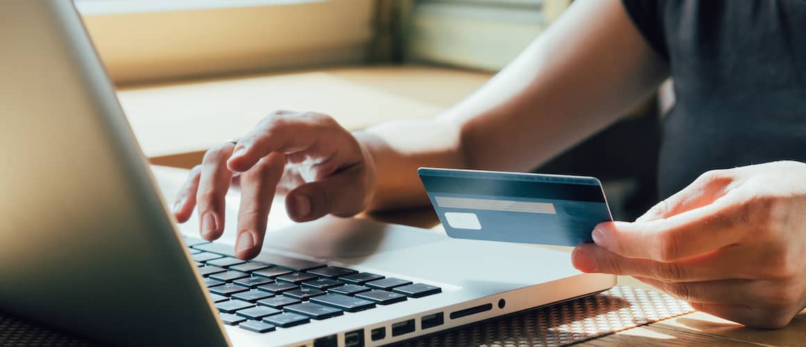 Close up view of someones hands holding a credit card as they also type on a laptop.