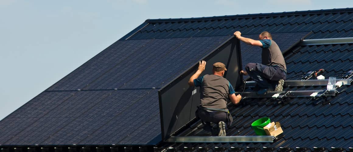 Two men installing modern black solar panels on a roof.