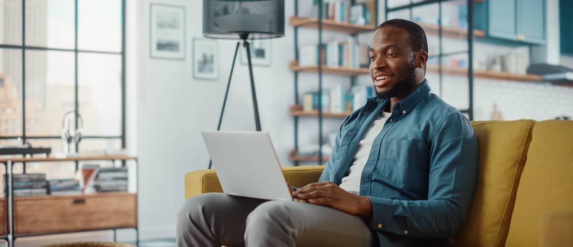 Black man sitting on couch looking at laptop.