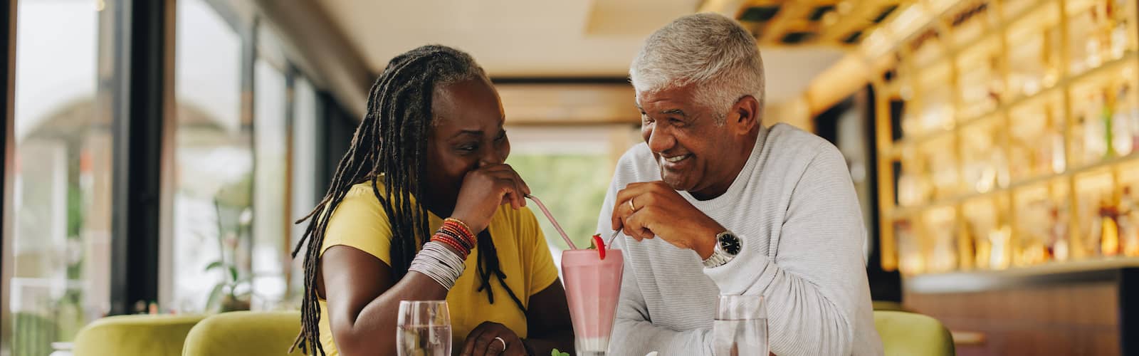 An African American senior couple enjoying a milkshake together at a cafe.