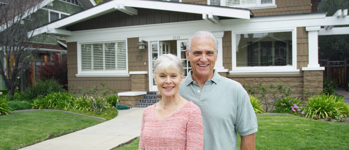 Older Couple standing next to their house.