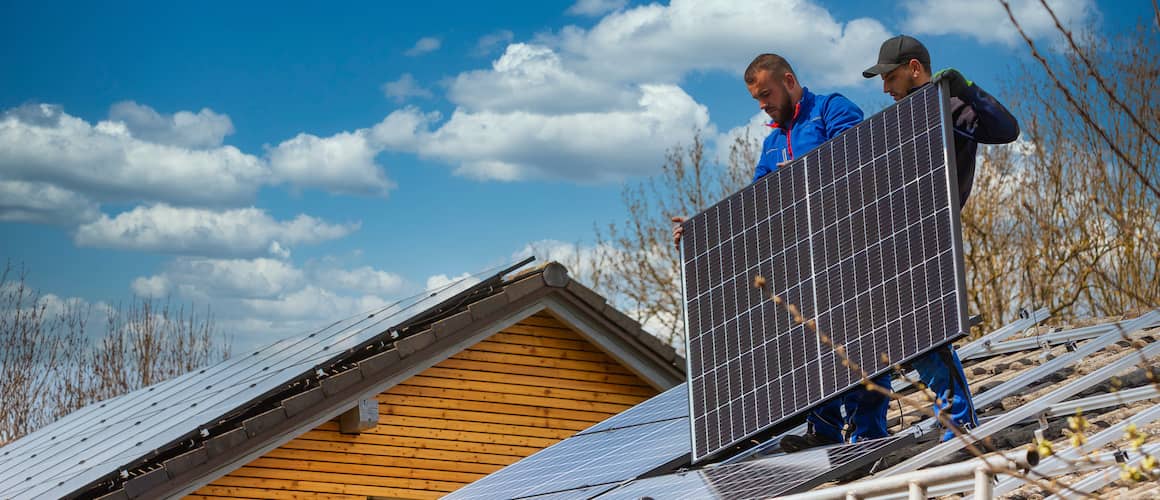 Two men installing more solar panels on roof.