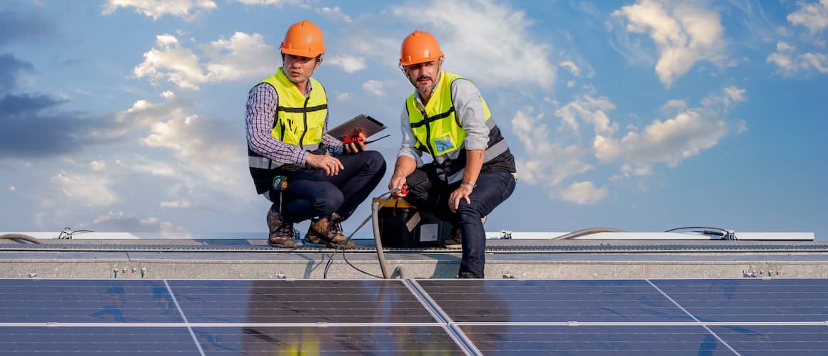 Two workers on solar panels during day.