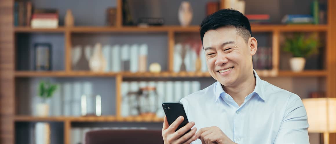 Asian man looking at phone wearing blue shirt.