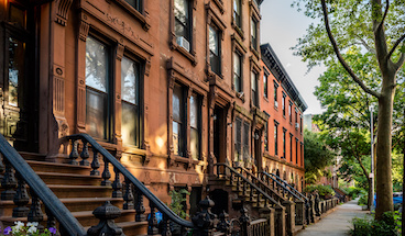 Scenic view of a classic Brooklyn brownstone block with a long facade and ornate stoop balustrades on a summer day in Clinton Hills, Brooklyn.