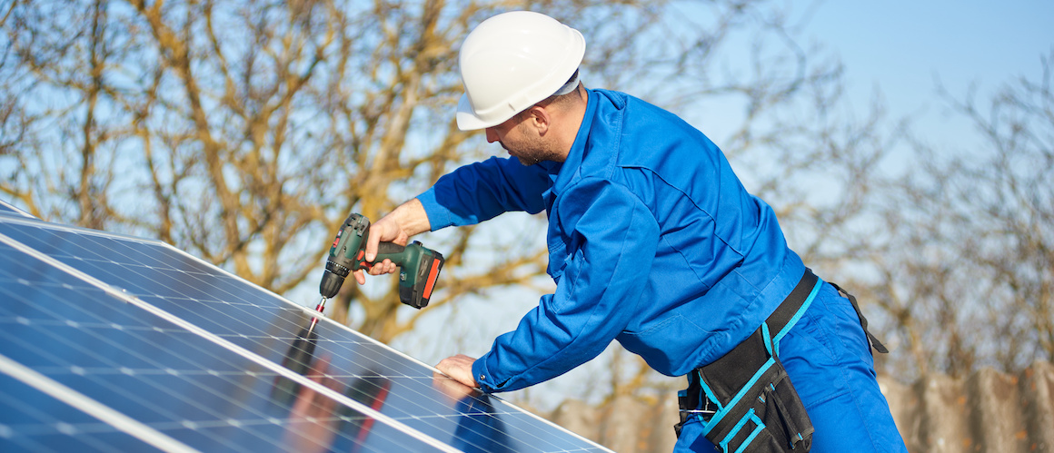 Man in blue uniform on roof installing solar panels on a sunny day.