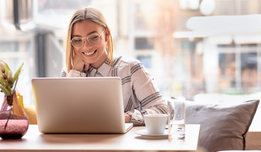 Woman wearing glasses on laptop in coffee shop.