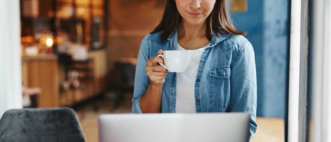 Female looking at laptop in cafe with coffee.